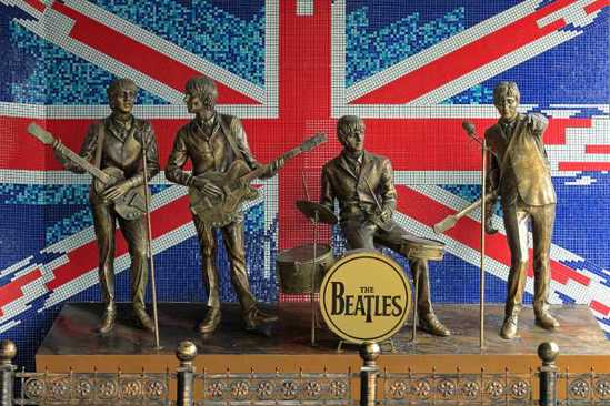 Brass statues of Beatles band members playing instruments in front of mosaic Union Jack wall