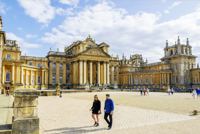 Two people walking across the gravel near entrance to Blenheim Palace on sunny day