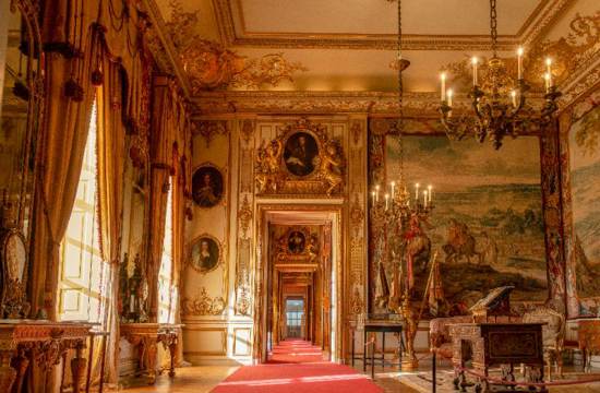 Sun streaming through windows in Blenheim Palace State Room, gold painted details around doors and red carpet running through doorway