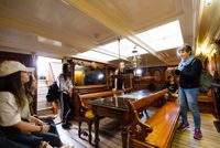 People stood in room onboard Cutty Sark, room has large wooden benches and a bright ceiling light