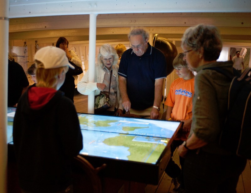 People stood around display at Cutty Sark, map which is back lit is in the centre of the room