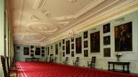 Room with red carpets and pale walls covered in paintings in frames at the Palace of Holyroodhouse