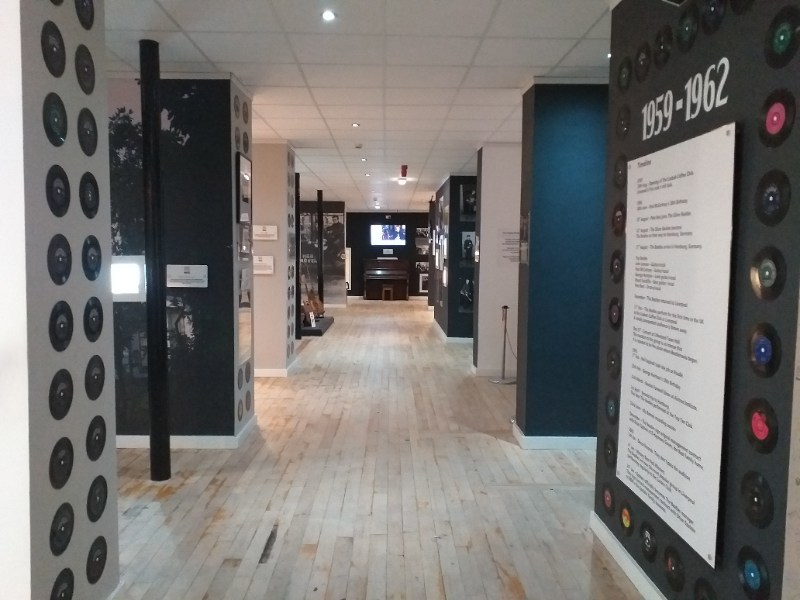 View down corridor at Liverpool Beatles Museum with pale wooden floors and dark blue painted walls covered in museum displays