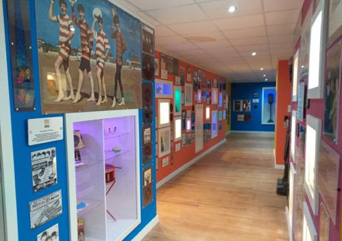 View down corridor at Liverpool Beatles Museum with pale wooden floors and dark blue painted walls covered in museum displays