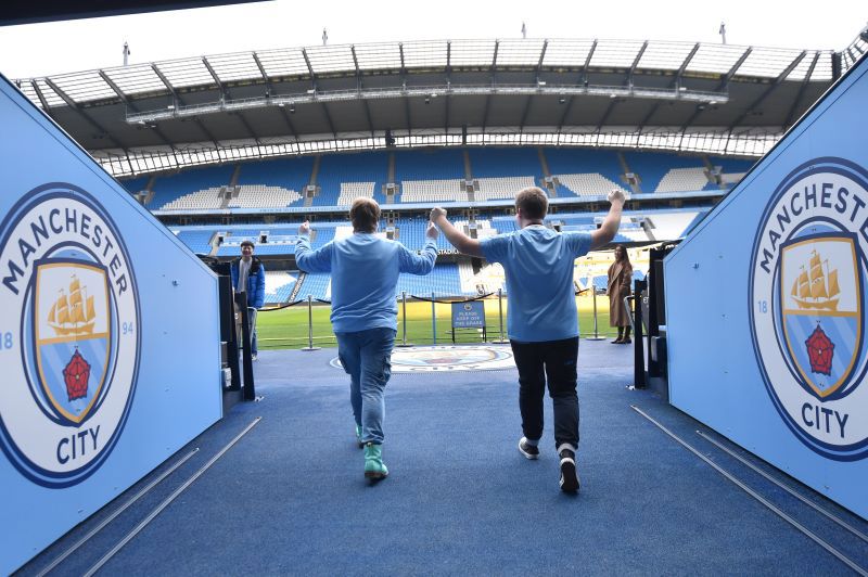 Two people running towards pitch with blue painted walls with Manchester City Football team logo