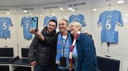 Three people taking selfie in front of Manchester City Stadium pitch