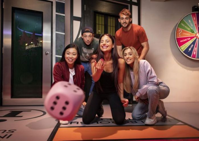 group of friends roll dice towards camera at monopoly lifesized