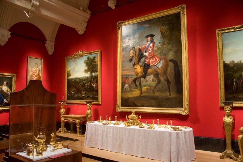 Room with bright red walls has a large portrait painting with gold frame in centre, behind white-clothed table