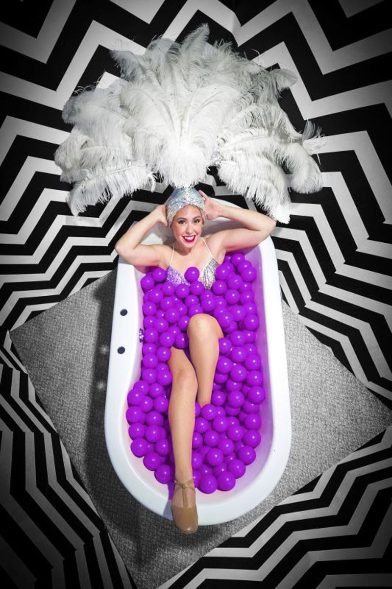 Woman posing in bath full of purple balls in room with chevron patterned walls at Selfie Town Blackpool