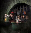 Man in tudor clothing holding a lantern in a boat of scared guests going through tunnel on the london dungeon tyrant boat ride